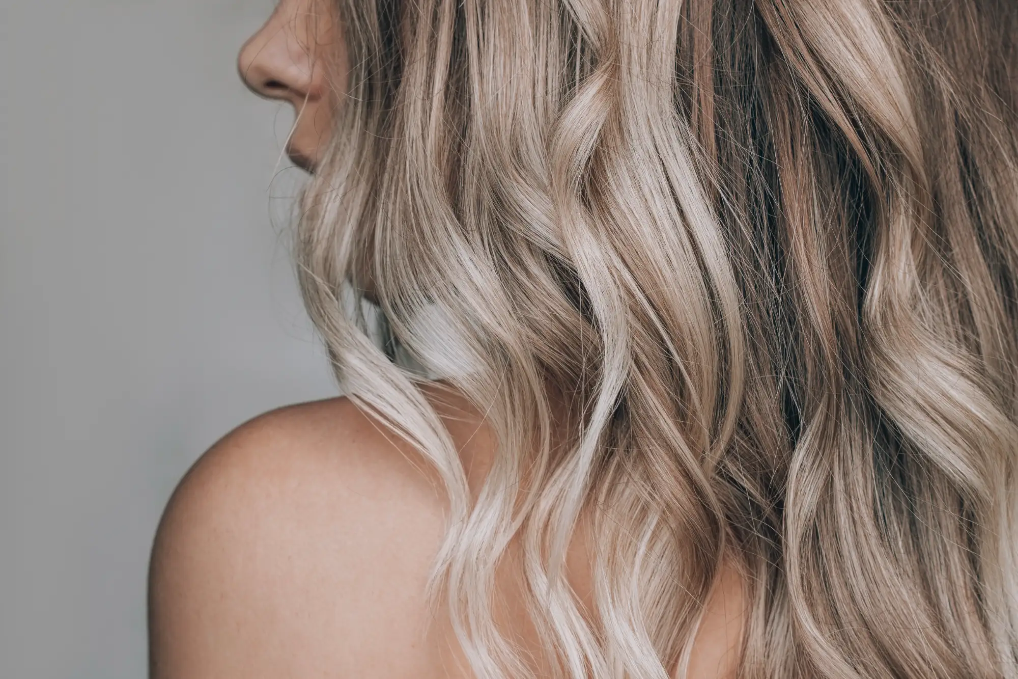 A person displays their long, wavy blonde hair with bright highlights and darker roots, fresh from a color treatment.