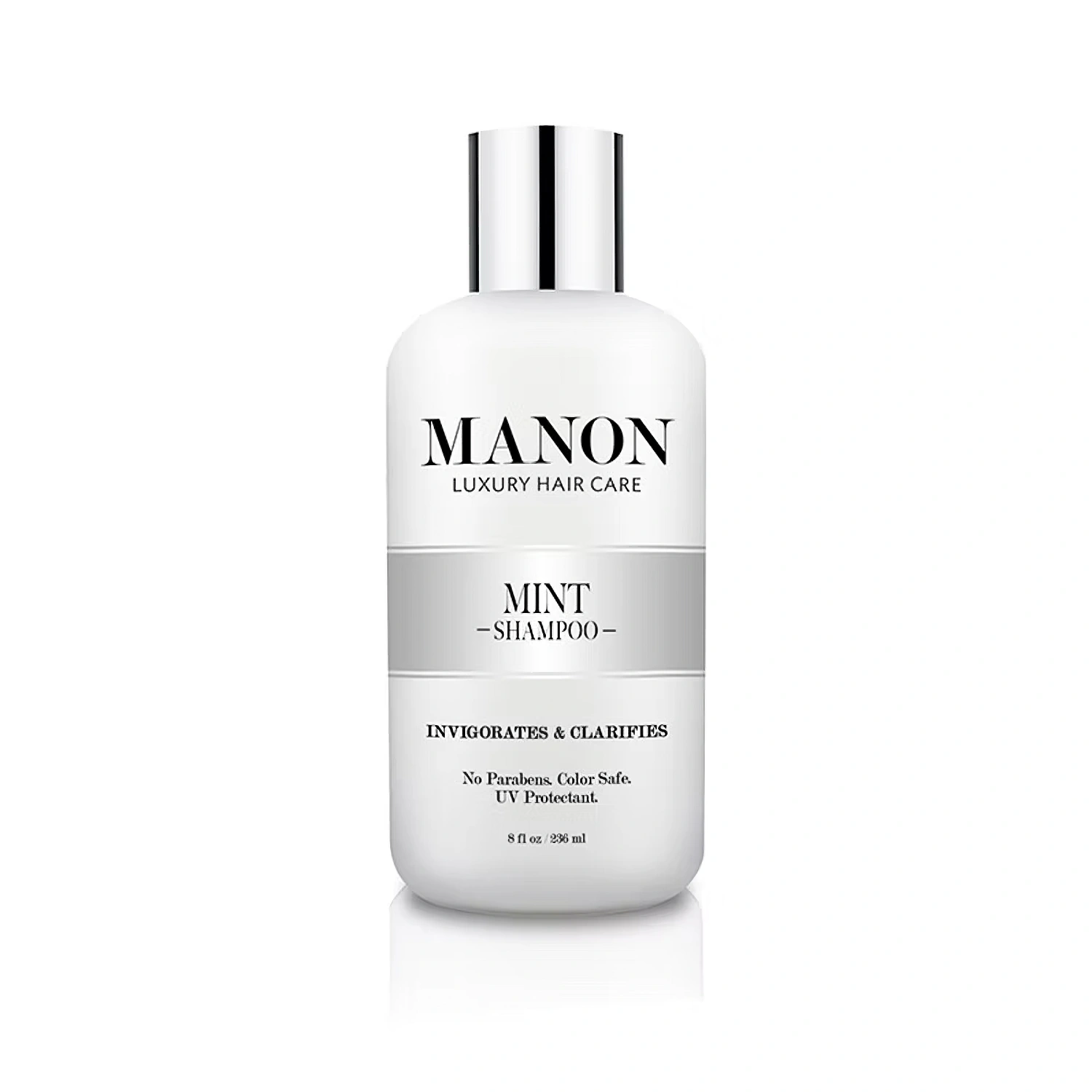 A white bottle of Manon Mint Shampoo, labeled "Invigorates & Clarifies," standing on a reflective surface against a white background.
