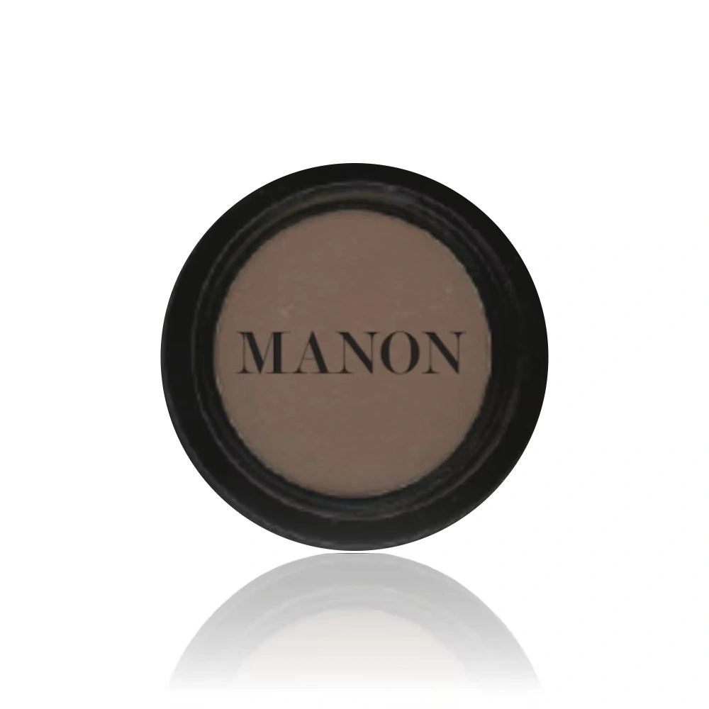 A circular pan of matte taupe blush powder, labeled "MANON," sitting in a black compact on a white background.