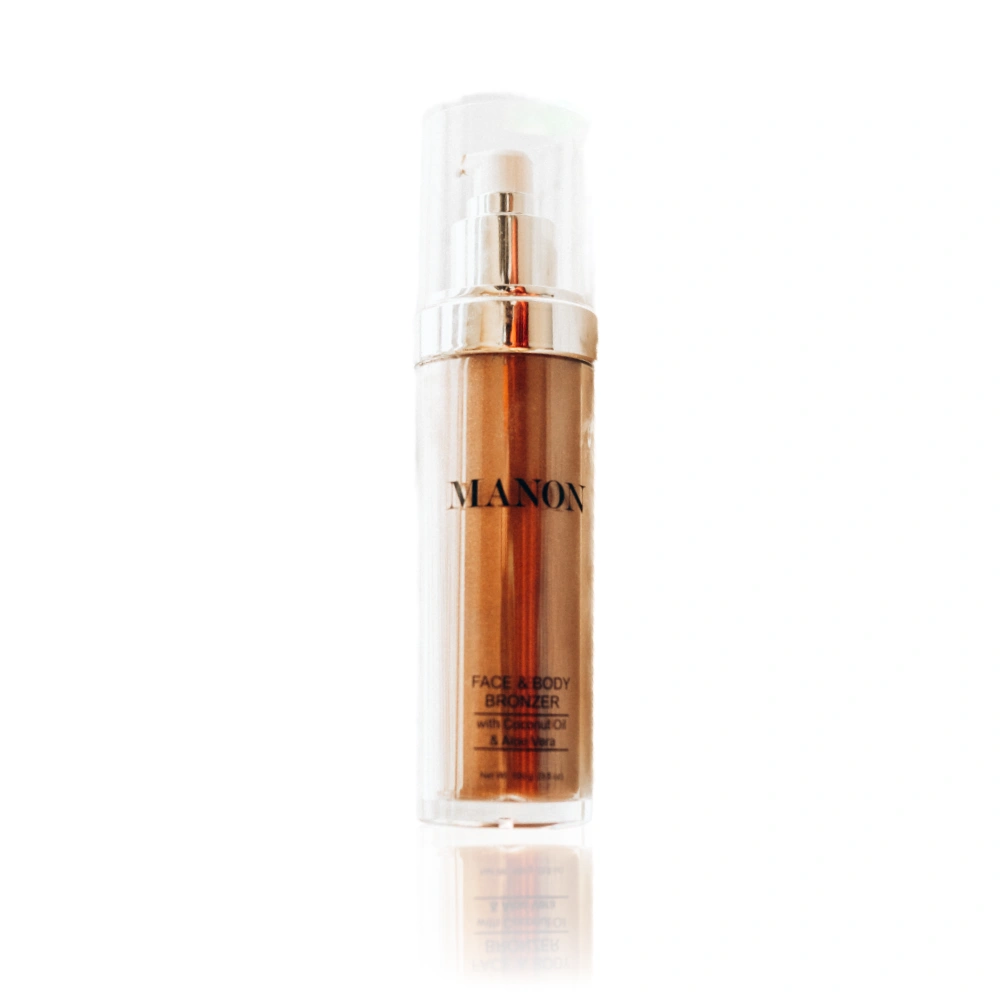 A clear bottle of Manon Face & Body Bronzer, a rich bronze liquid with a pump dispenser, displayed on a white background.