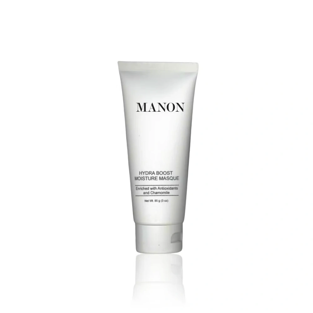 A white tube of Manon Hydra Boost Moisture Masque, enriched with Antioxidants and Chamomile, reflecting lightly on a white surface.