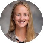 Claire DeBoer smiles in a professional headshot. She has blonde hair and is wearing a plaid blazer over a white blouse with a black bow.