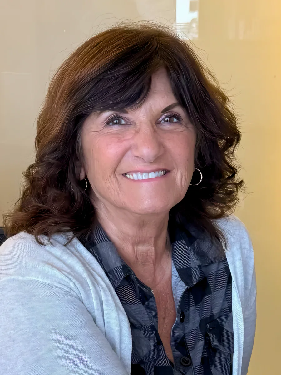 Amy Ayan, Front Desk Coordinator, smiling warmly, appears ready to assist clients. She wears a gray cardigan.