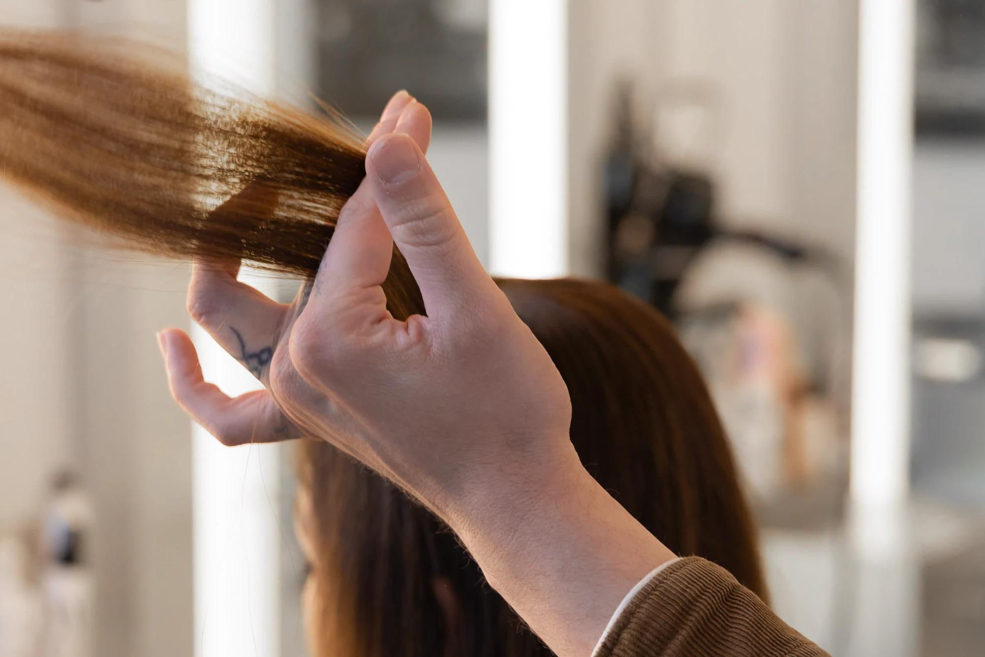 Stylist Matthew holds a section of long brown hair between his fingers, preparing to give a haircut in the salon.