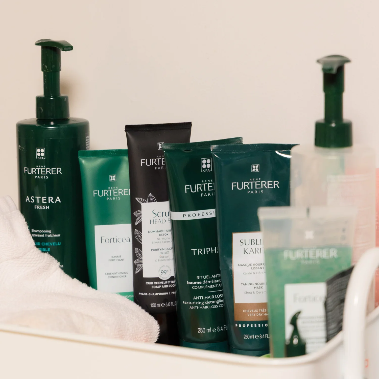 A collection of dark green René Furterer hair care products, including shampoos and conditioning masks, arranged neatly in a white storage tray next to a white towel.